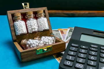 Obraz na płótnie Canvas Wooden box with homeopathic medicine glass bottles and calculator, Indian rupees on blue and dark background - Money and Medicine concept