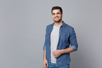 Handsome stylish unshaven young man in denim jeans shirt posing isolated on grey wall background...