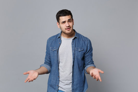Angry mad sad upset unshaven young man in denim jeans shirt posing isolated on grey wall background studio portrait. People sincere emotions lifestyle concept. Mock up copy space. Screaming gesturing.