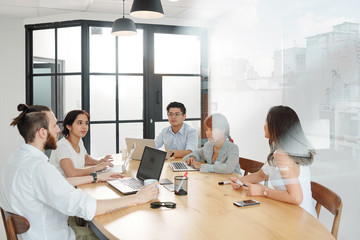 Group of multiethnic business people sitting at the table and discussing future business plans during meeting at board room