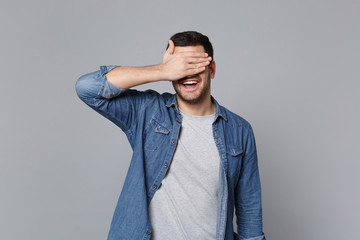 Handsome stylish unshaven young man in denim jeans shirt posing isolated on grey wall background...