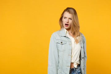 Fototapeta premium Portrait of shocked perplexed young woman in denim casual clothes standing and looking aside isolated on bright yellow orange wall background in studio. People lifestyle concept. Mock up copy space.