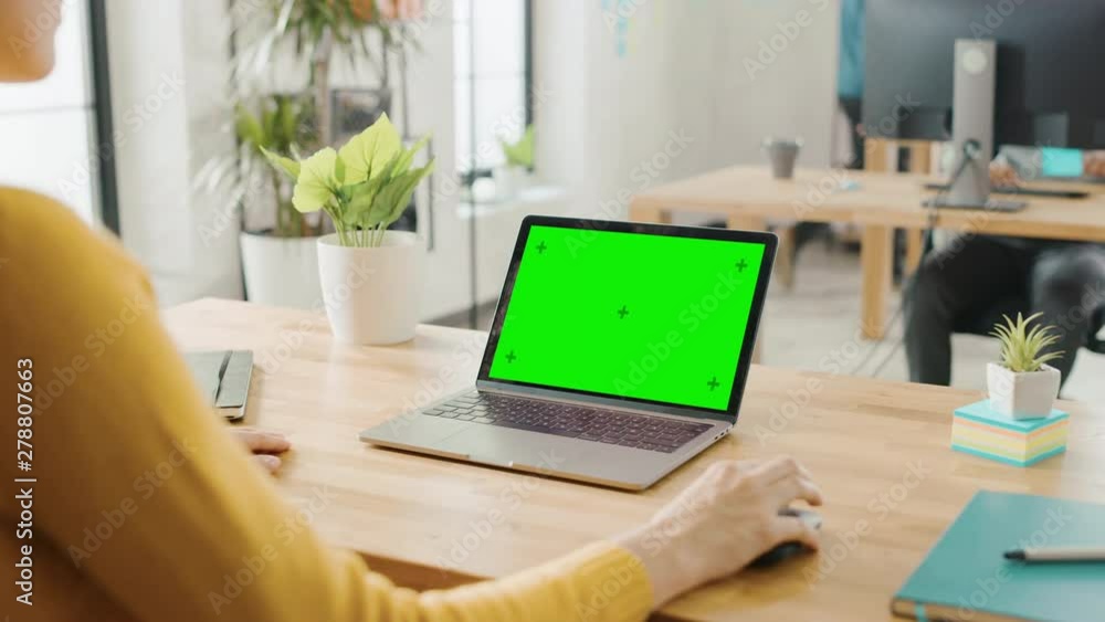 Aufkleber over the shoulder: creative young woman sitting at her desk using laptop with mock-up green screen. 