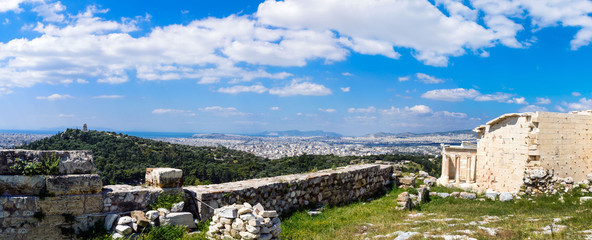 Fototapeta premium Ancient Greek ruins, ruins amidst lush green grass. Acropolis, Athens, Greece. Beautiful view of the capital of Greece - Athens from the slopes of the Acropolis on a hot sunny day. Panorama.