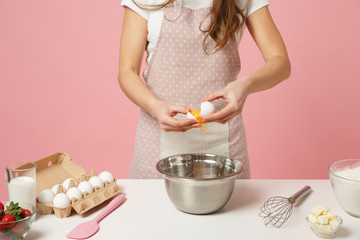 Close up cropped female chef cook confectioner or baker in apron white t-shirt cooking cake or cupcake at table hold eggs isolated on pink pastel background in studio. Mock up copy space food concept.