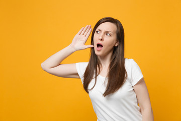 Portrait of curious young woman in white casual clothes looking aside try to hear you with hand...