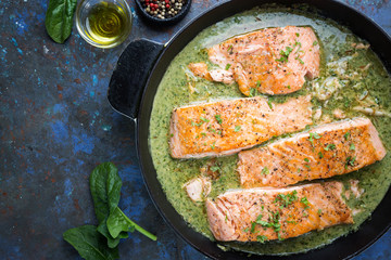 Grilled Salmon with spinach and garlic cream sauce in a frying pan, top view