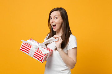 Pretty young woman in white casual clothes hold red striped present box with gift ribbon isolated...