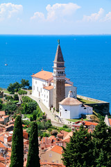 View of St George's Church and the red tiled rooftops of the old town of Piran in Slovenia, with...
