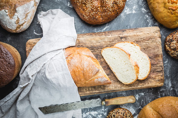 Assortment of fresh baked bread and buns on black background, top view