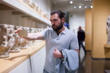 Adult male visitor using phone in sculptures exposition at museum