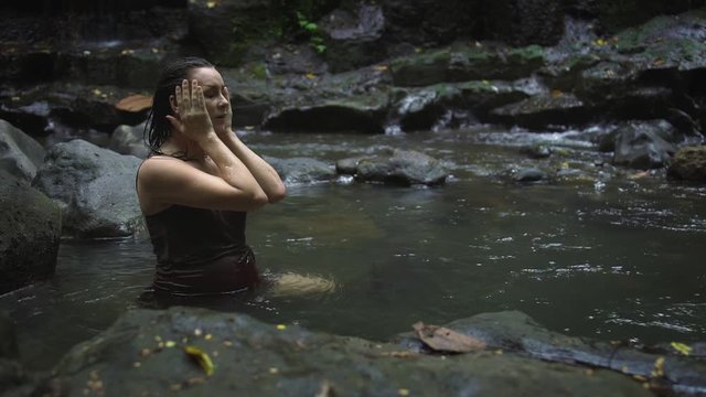 Beautiful pregnant woman in a dark brown dress bathing in the tropical jungle river. Slow motion.