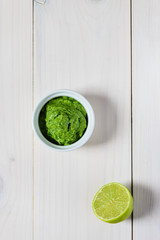 Guacamole from avocado, lime, cilantro and garlic  in white bowl on wooden table. Flat lay, closeup.