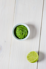 Guacamole from avocado, lime, cilantro and garlic  in white bowl on wooden table. Flat lay, closeup.