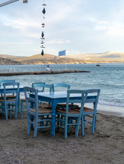 Traditional greek tavern with wooden tables on sandy beach near water waiting for tourists in Tolo,...