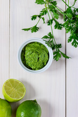 Guacamole from avocado, lime, cilantro and garlic  in white bowl on wooden table. Flat lay, closeup.