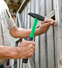 To hammer a nail with a hammer. Older worker carpenter