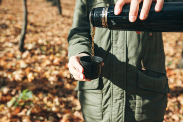 Person with a thermos in his hands in the autumn forest. The man is going to drink goyang drink - tea or coffee to keep warm.