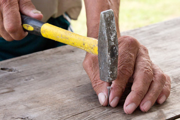 To hammer a nail with a hammer. Older worker carpenter