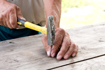 To hammer a nail with a hammer. Older worker carpenter