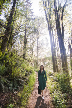 Portrait of young woman with bag walking on forest road