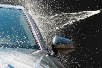 Сar washing with high pressure water jet. Water and foam under pressure flies toward the car body. Close-up view