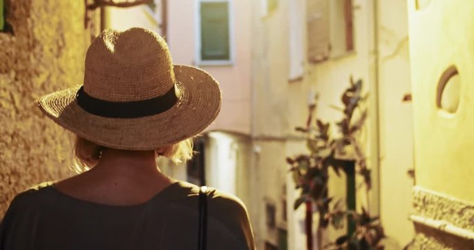 Beautiful romantic girl exploring old vintage city during summer tour. Following a stylish woman in sun hat walking in narrow street of Rio Majore village. Travel to Italy.