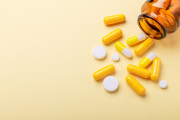 Multicolor tablets and pills capsules from glass bottle on yellow background Heap of assorted various medicine tablets and pills. Health care Close-up Copy space