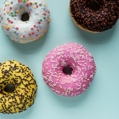 Top view of assorted donuts with chocolate frosted, pink glazed and sprinkles on a blue background.