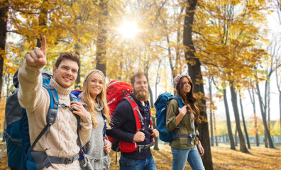 travel, tourism and hike concept - group of smiling friends walking with backpacks over autumn park...