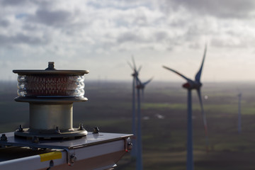 Close-up of aviation light on a wind turbine with blurry wind farm in the background