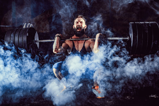 Muscular bearded tattoed fitness man doing deadlift a barbell over his head in modern fitness center. Functional training. Snatch exercise