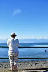 Woman walking alongside seawall stopping to admire the ocean view on beautiful summer day