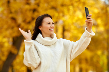 season, technology and people concept - beautiful young happy woman taking selfie by smartphone at autumn park