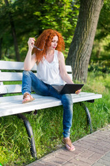 Naklejka premium Red-haired female freelancer working on a laptop while sitting on a park bench.