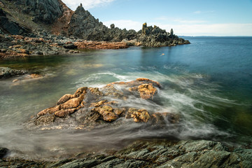 Fototapeta na wymiar Seascape with silky waves washing over the rugged rocky coast. Atlantic coast of Newfoundland. 