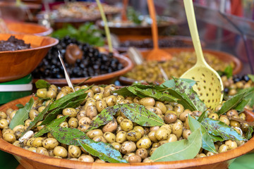 Close-up fresh olives in bowl with wooden spoons for sale at a stall street market in Provence...