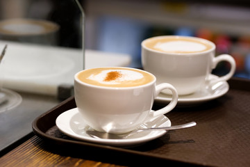 Two cups of cappuccino with latte art on wooden background. Beautiful foam, greenery ceramic cups, stylish toning