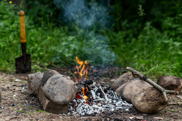 The sharp used spade is stuck in the ground with grass near a campfire