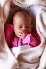 Cute newborn baby in pink baud is sleeping on her bed under beige blanket.