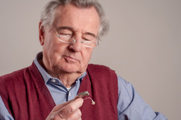 Worried senior man holding hearing aid 