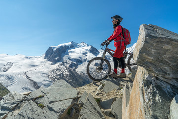 active senior woman, riding her electric mountainbikeon the Gornergrat in Zermatt, Wallis,Switzerland. In The background Gorner Glacier, Monte Rosa, Liskam am Breithorn