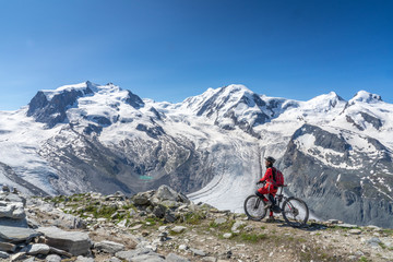 Fototapeta na wymiar active senior woman, riding her electric mountainbikeon the Gornergrat in Zermatt, Wallis,Switzerland. In The background Gorner Glacier, Monte Rosa, Liskam am Breithorn