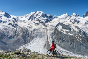 Fototapeta na wymiar active senior woman, riding her electric mountainbikeon the Gornergrat in Zermatt, Wallis,Switzerland. In The background Gorner Glacier, Monte Rosa, Liskam am Breithorn