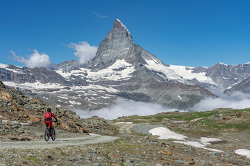 active senior woman, riding her electric mountainbike below the famous Matterhorn in Zermatt,...
