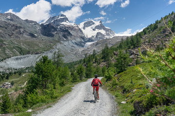 Fototapeta na wymiar active senior woman, riding her electric mountain bike below the Gornergrat in Zermat, Canton Valais, Switzerland, in The background Rimpfischhorn and Strahlhorn
