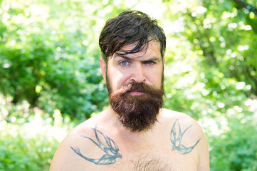 The masculine nature. Masculine guy with tattoo on shoulders on summer landscape. Bearded man...