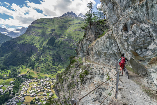 Active Senior Woman, Pushing Her Electric Mountain Bike On A Narrow Mountain Bike Trail High Above Zermatt, The Famous Touristic Destination In The Swis Alps, Canton Valais, Wallis, 