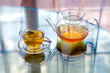 Transparent glass tea cup and pot with spoon on glass table in strong backlit