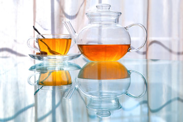 Transparent glass tea cup and pot with spoon on glass table in strong backlit